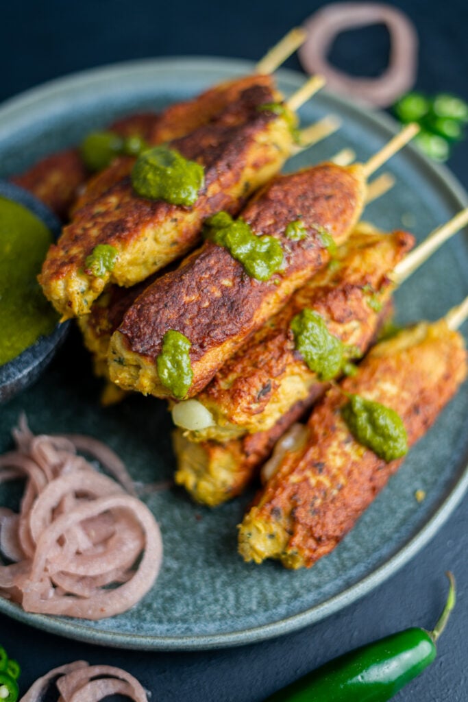 a stack of chicken seekh kebabs with a drizzle of cilantro-mint chutney and pickled purple onions