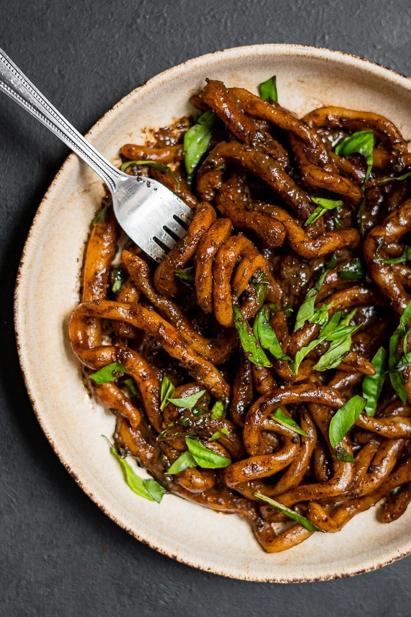 Black Garlic Pici on Black Background with Shredded Basil and a fork twirling noodles