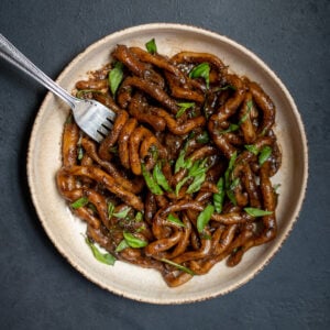 Black Garlic Pici on Black Background with Shredded Basil