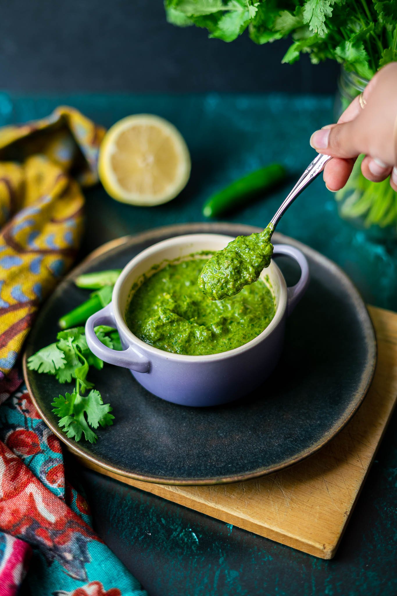 spooning up cilantro-mint chutney from a purple mini le creuset dutch oven in a black plate with cilantro and serrano peppers