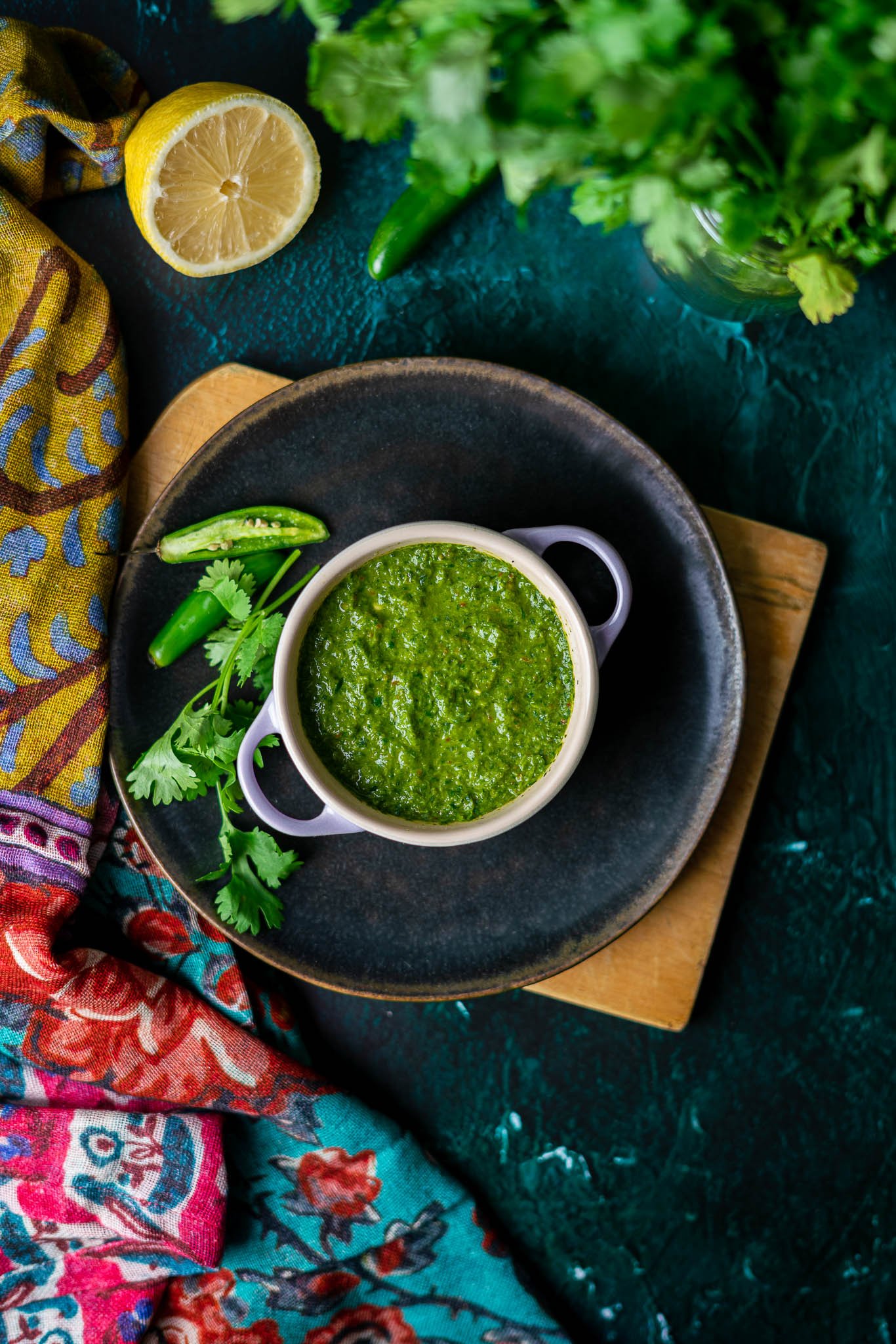 a flatlay of cilantro mint chutney in a mini dutch oven on a black plate with serrano peppers and cilantro