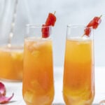 Tropical Guava Sangria in fluted glasses side by side with lychees, guava paste, and pitcher in the background