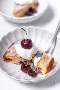 amaretto cherry almond cake in bowl with whipped cream and cherries dug into with a spoon