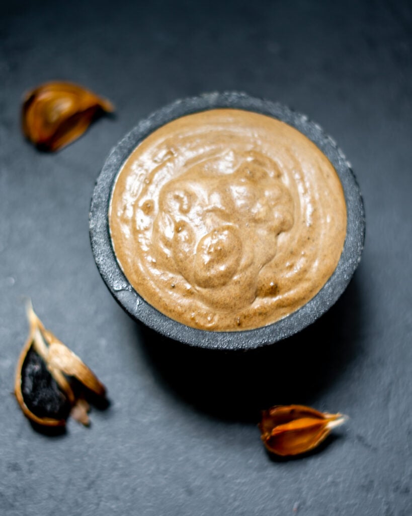 creamy black garlic sauce in a small bowl with black garlic cloves