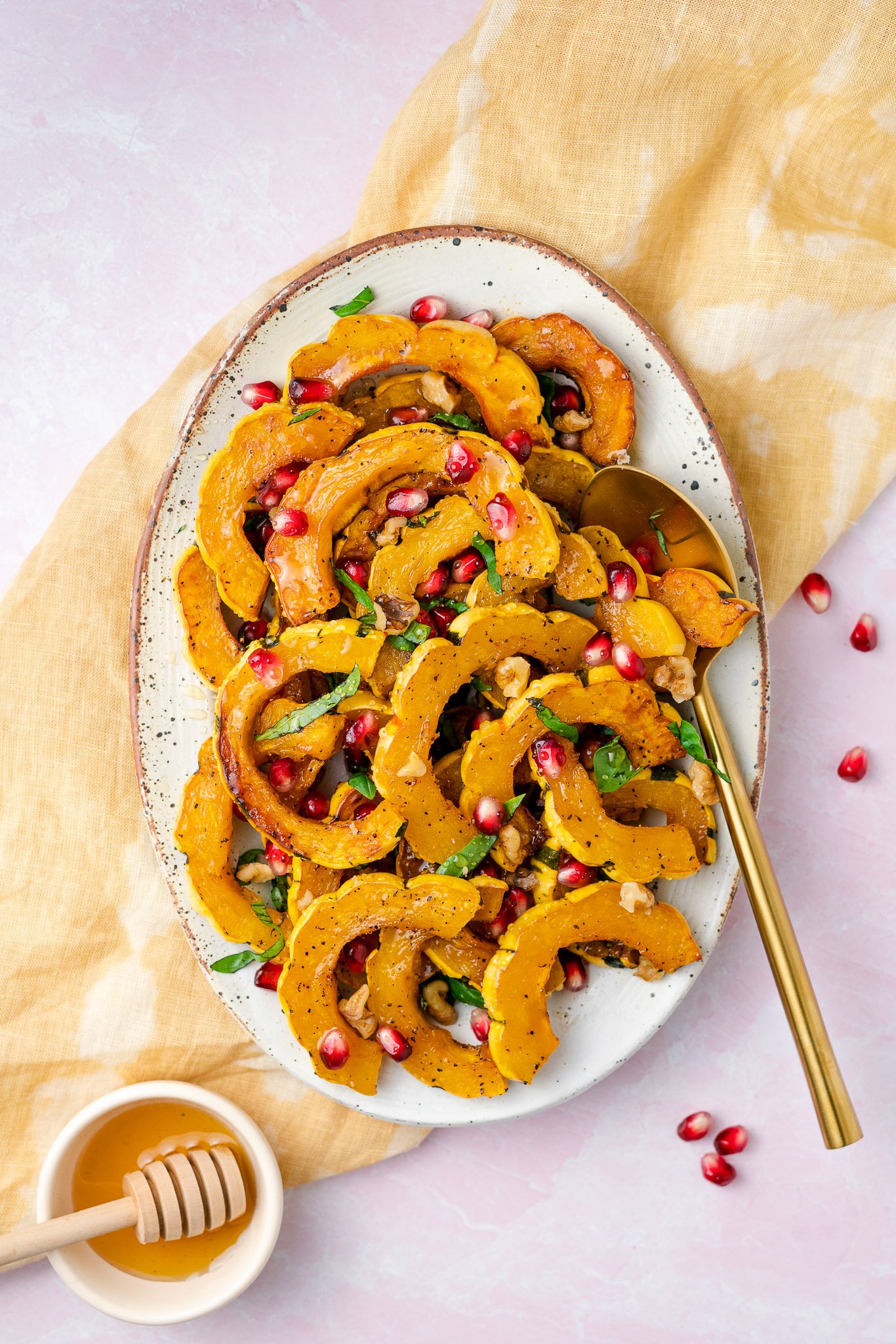 Delicata Squash with Pomegranates, Walnuts, and Basil in a platter with a golden spoon and honey in a bowl