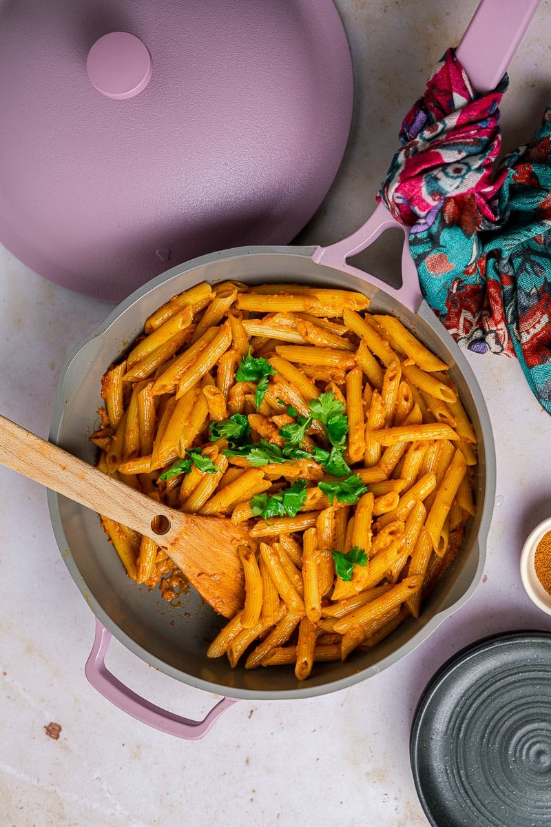 Butter Masala Pasta in a lavender always pan with cilantro garnish and a wooden serving spoon