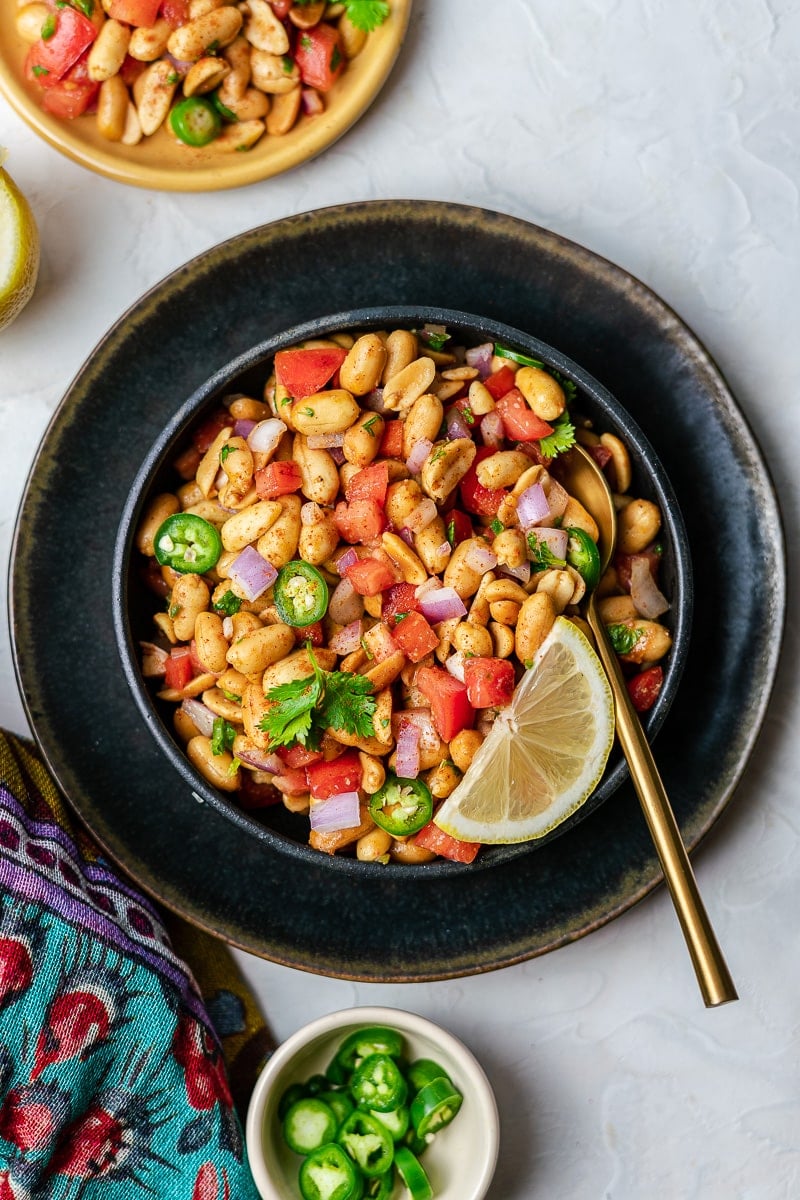 peanut chaat in black bowl on black plate with chili peppers and an extra plate