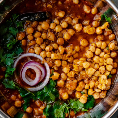 close up shot of chole in a flat bottomed wok with red onion and cilantro garnish