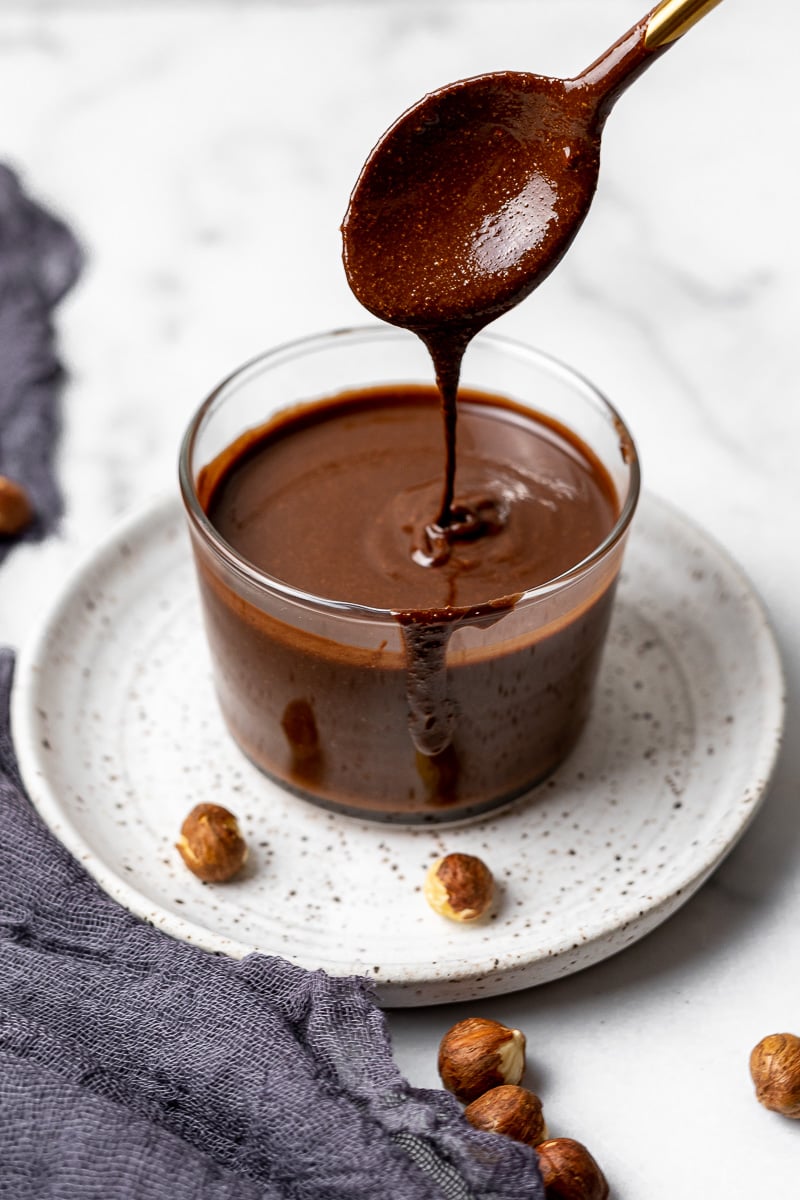 spooning up Homemade Nutella in glass jar with raw hazelnuts