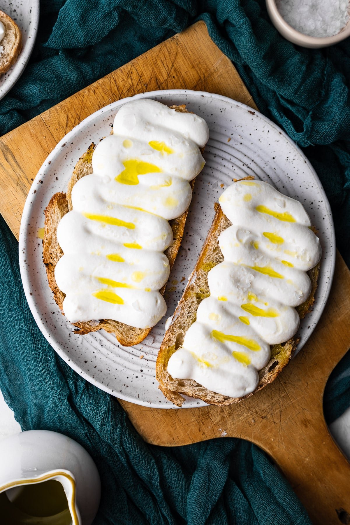 two slices of whipped ricotta toast on a plate on a brown wooden board.