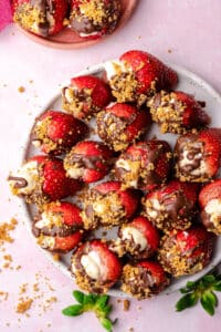 strawberries stuffed with cheesecake topped with chocolate and graham crackers in a plate