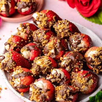 strawberries stuffed with cheesecake topped with chocolate and graham crackers in a plate with a rose