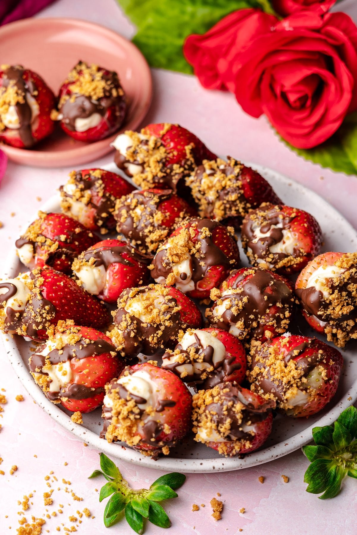 strawberries stuffed with cheesecake topped with chocolate and graham crackers in a plate with a rose