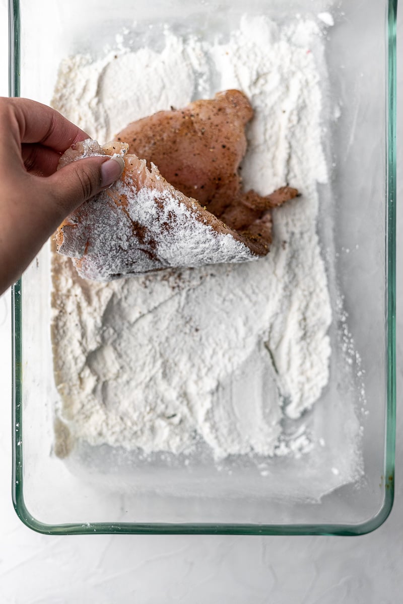 a slice of chicken rubbed in garam masala being dredged in flour in a glass container