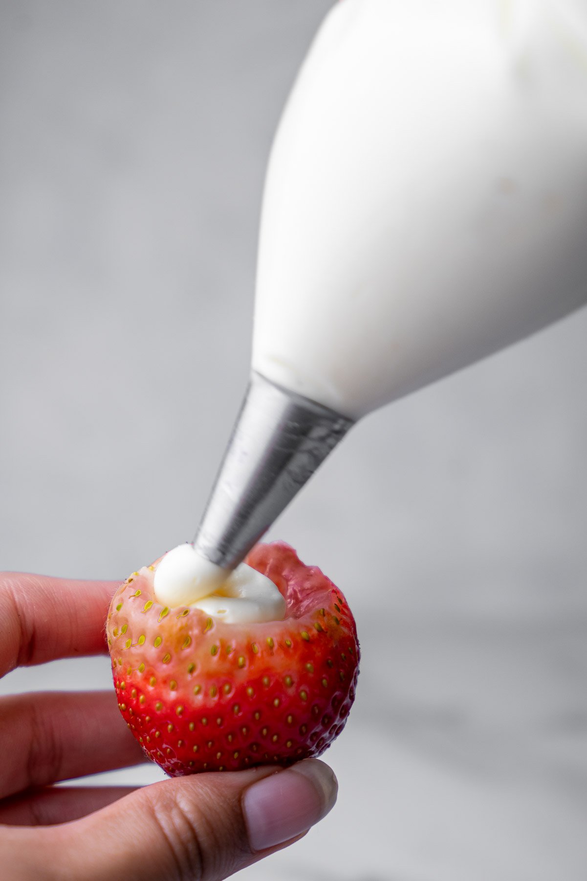 a single hollowed strawberry being filled with cheesecake filling from a piping bag