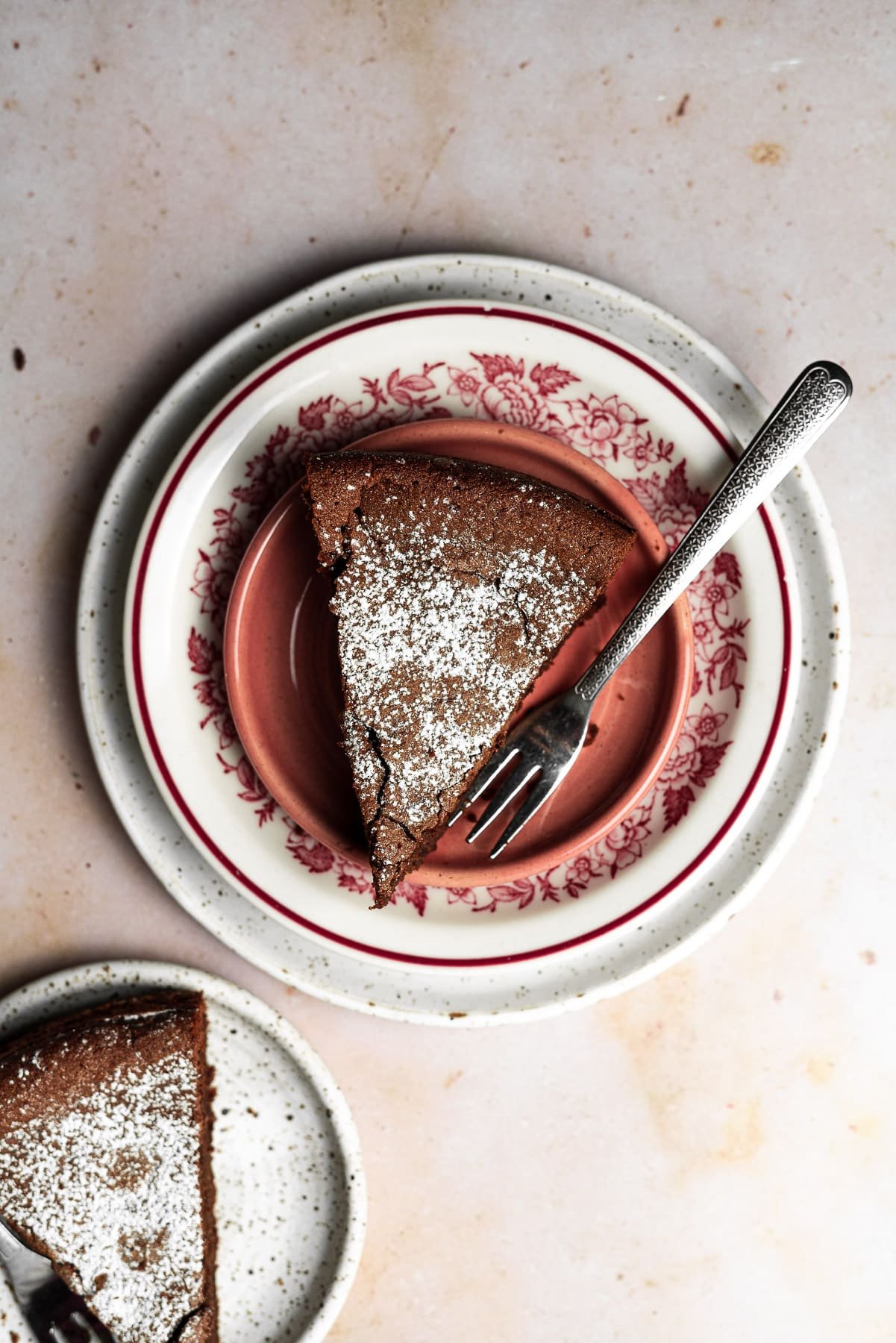 a single slice of flourless nutella cake on stacked plates with another slice on the bottom left