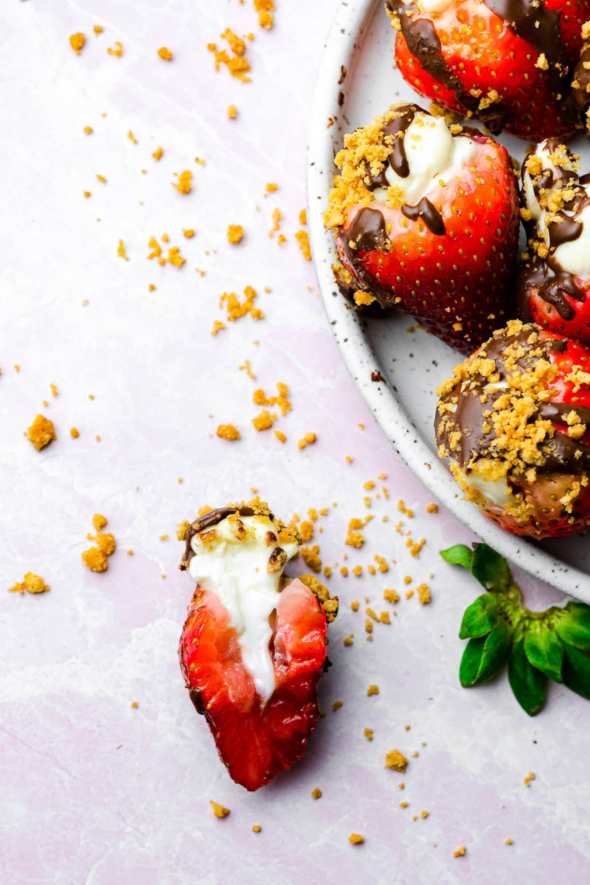 a single strawberry halved to show a cheesecake filling amongst crumbs and a plate of similar strawberries