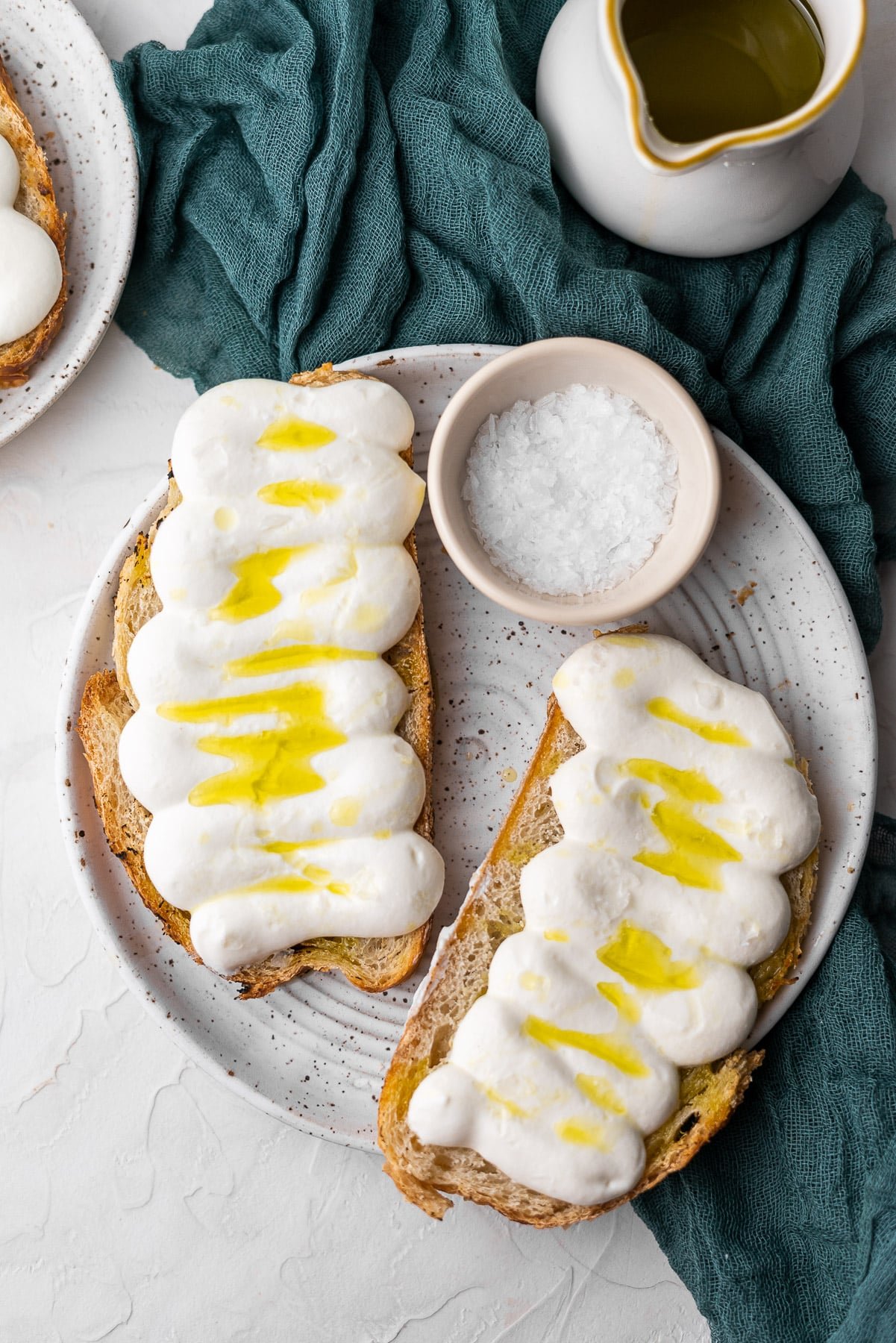 two slices of whipped ricotta toast on a plate with flaky salt.