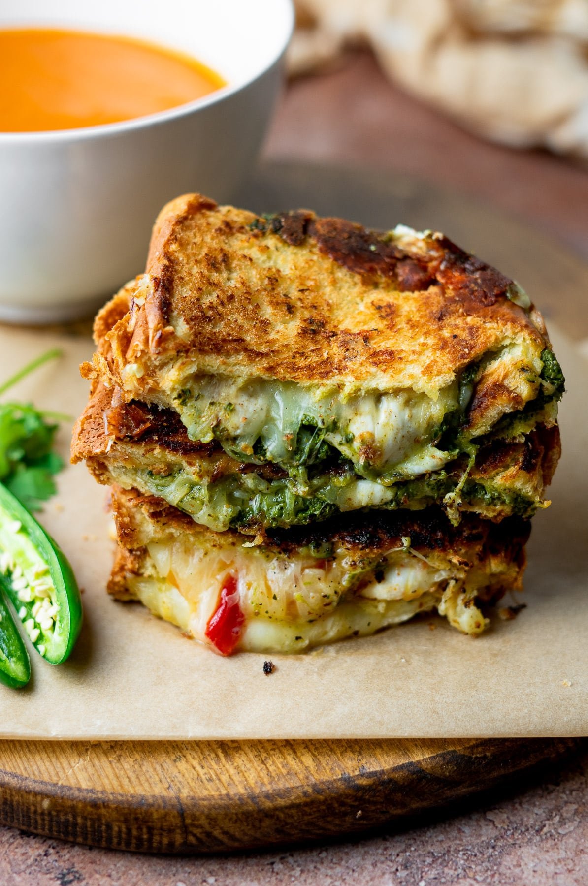 stack of grilled cheeses on a wooden board with tomato soup