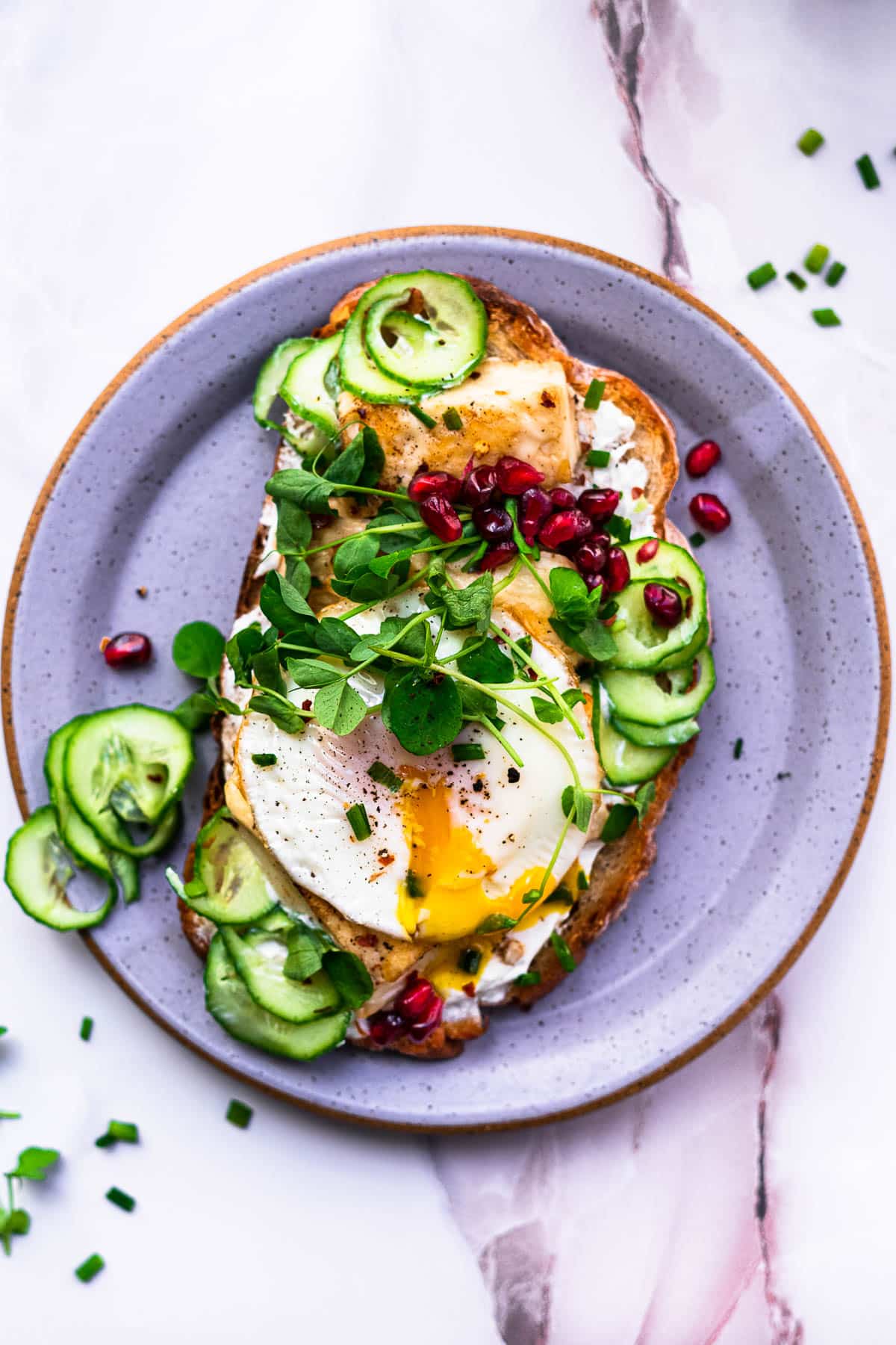 egg, cucumber, pomegranates, halloumi, chives, and labneh on homemade toast on a purple plate