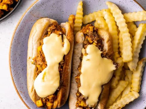 paneer filling on a hot dog bun with cheese sauce and crinkle fries on the side