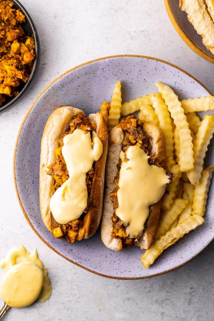 paneer filling on a hot dog bun with cheese sauce and crinkle fries on the side