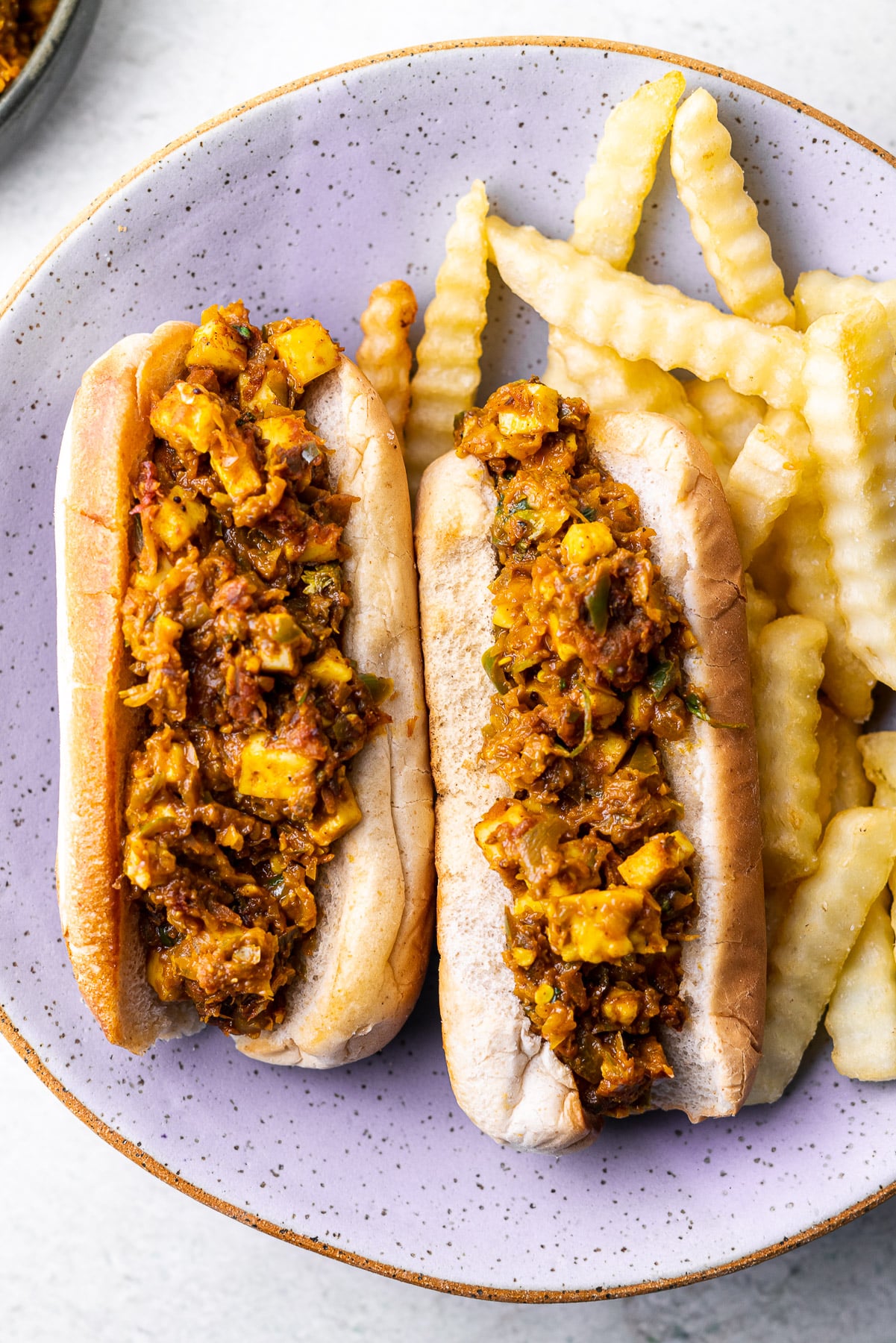 Paneer Masala Filling in hot dog with crinkle fries on a purple plate