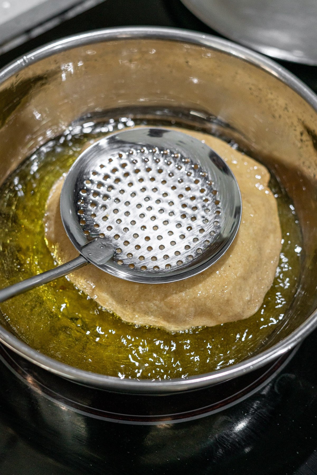 Bhatura being fried in oil with a slotted spoon pressing it down in the oil