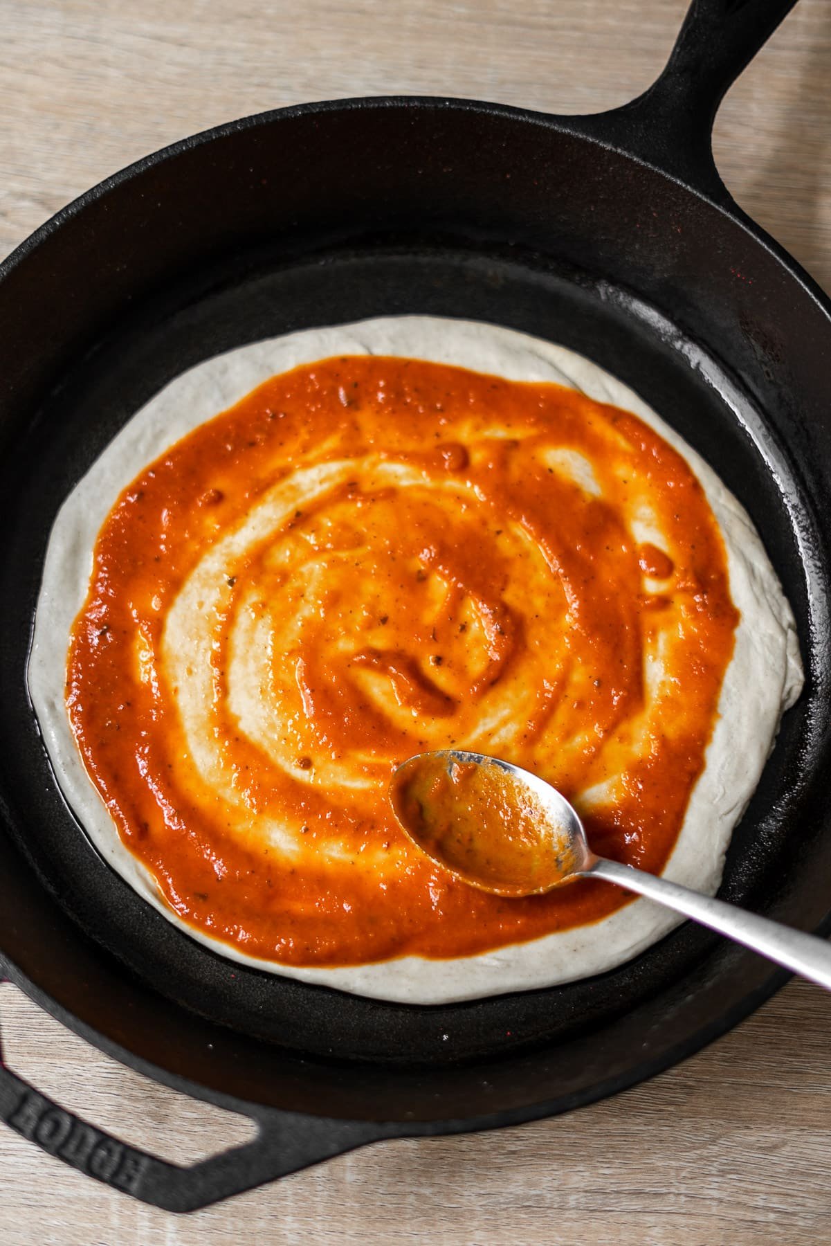 Pizza Dough Unbaked with sauce spread by a spoon in a cast iron pan