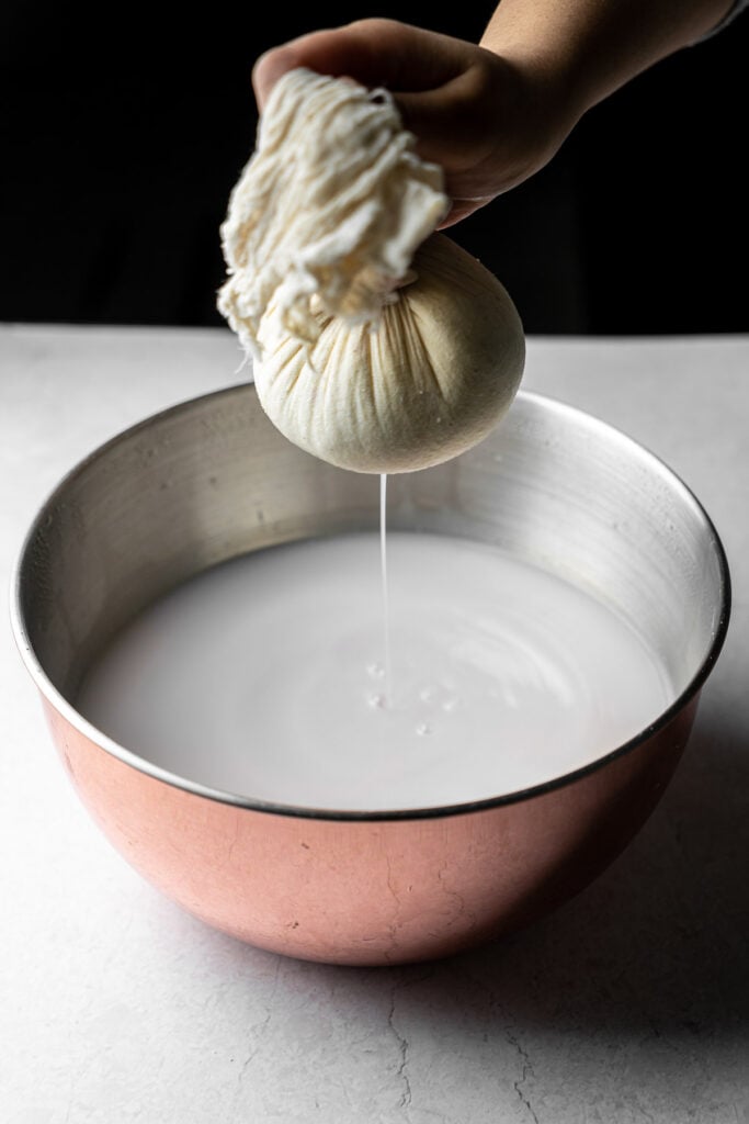 milk curds in a cheese cloth with whey being strained into a large bowl full of whey
