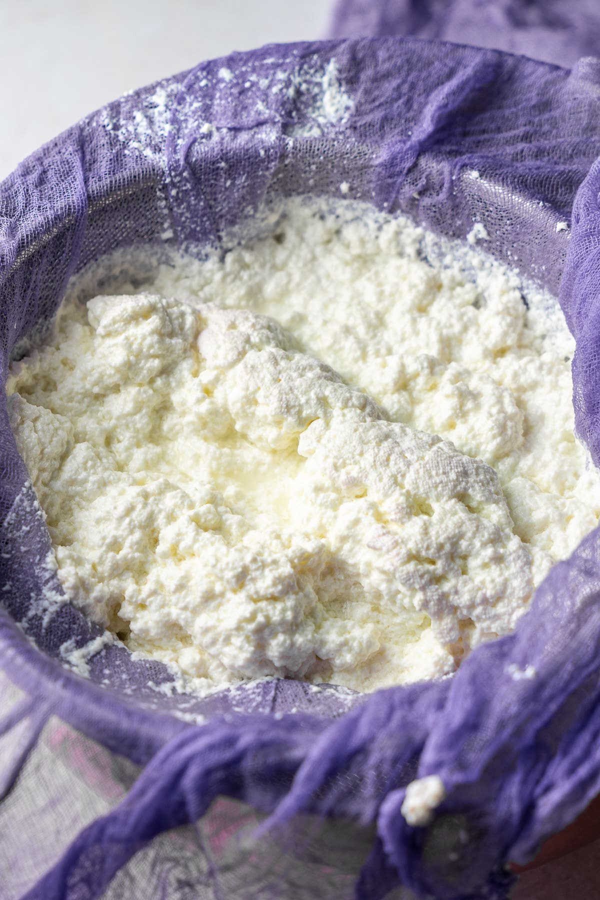 loose milk curds being strained into a bowl over a cheesecloth
