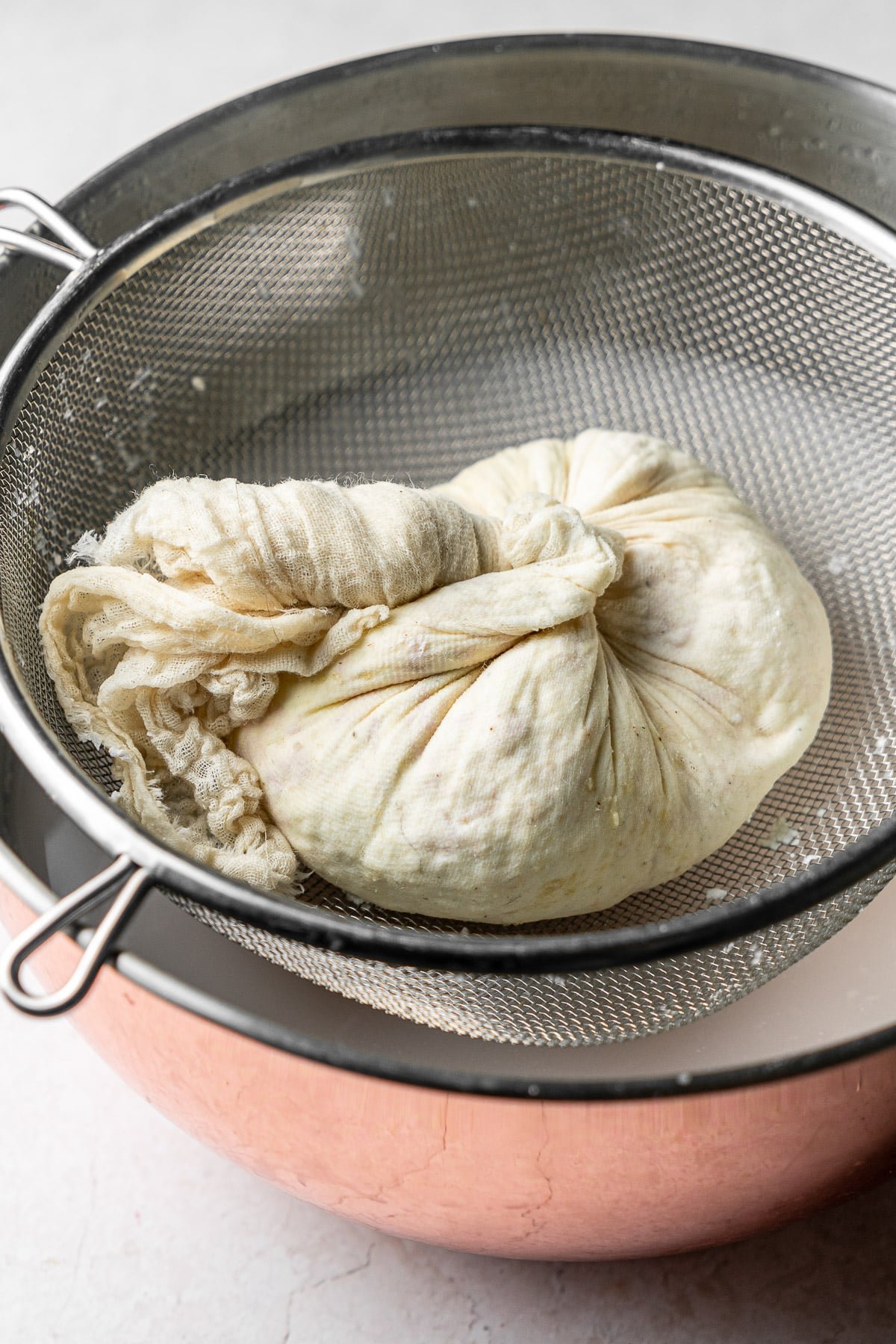 milk curds collected in a cheese cloth on a strainer over a bowl