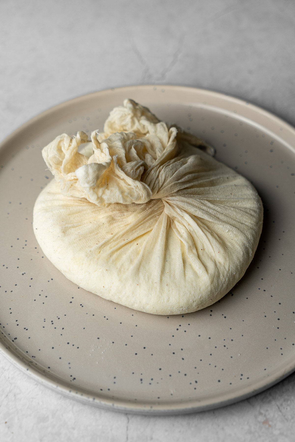 a block of paneer in a cheese cloth on a plate after being pressed