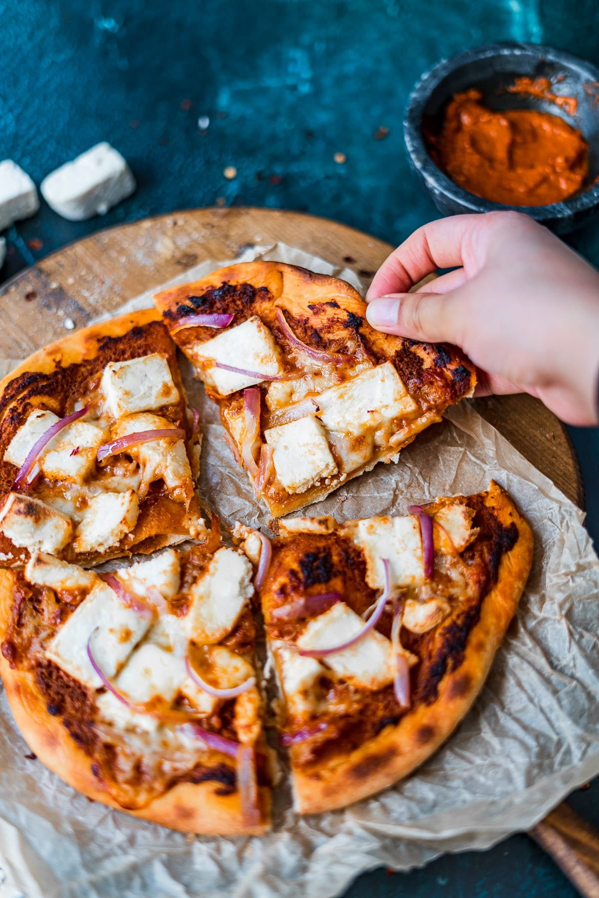 a hand grabbing a slice of paneer makhani pizza