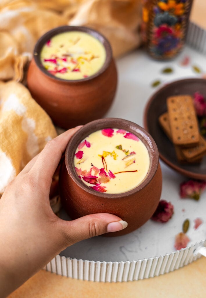 hand grabbing a cup of thandai in chai cups on a white tray