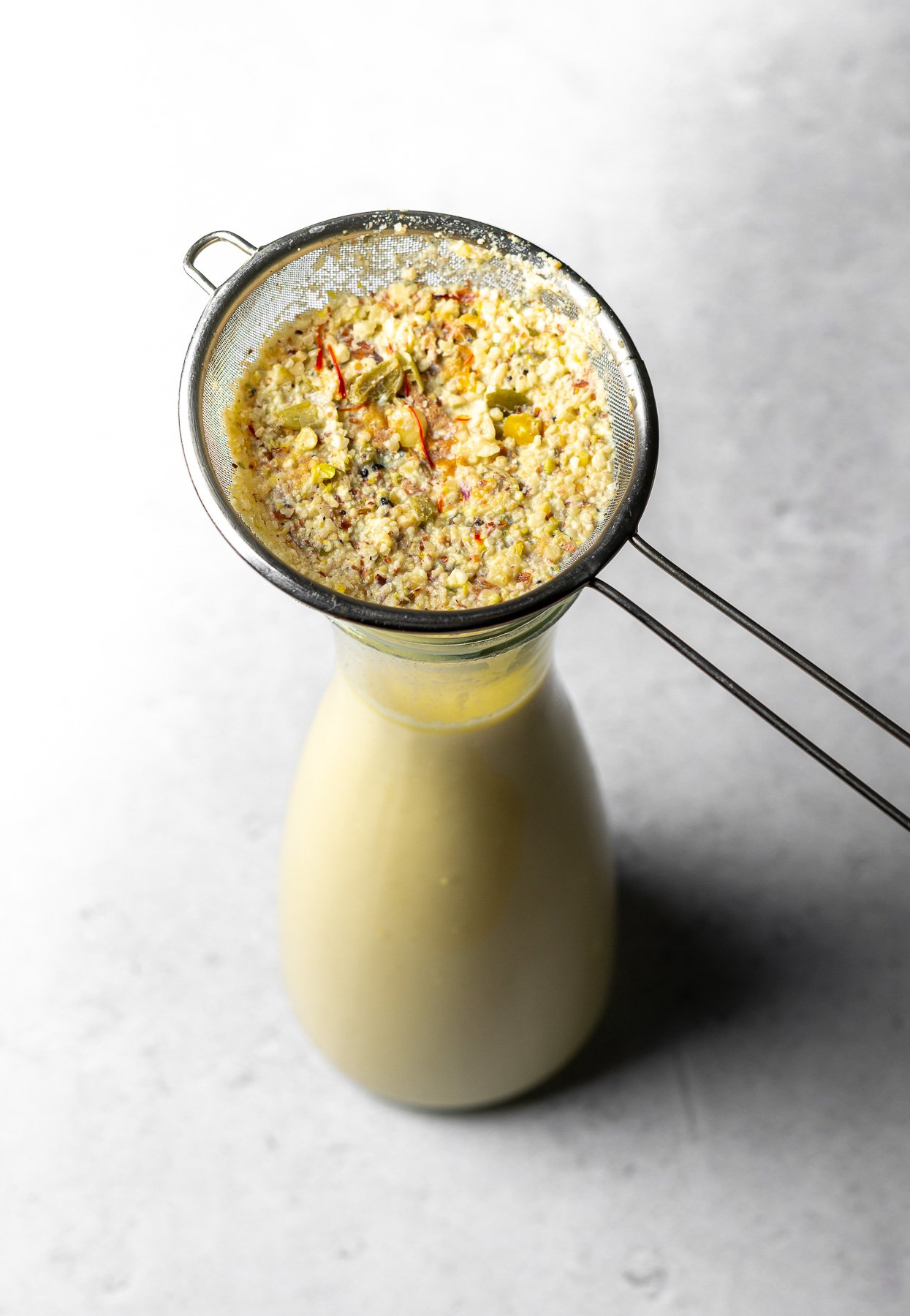 Straining masala out of thandai and into a pitcher