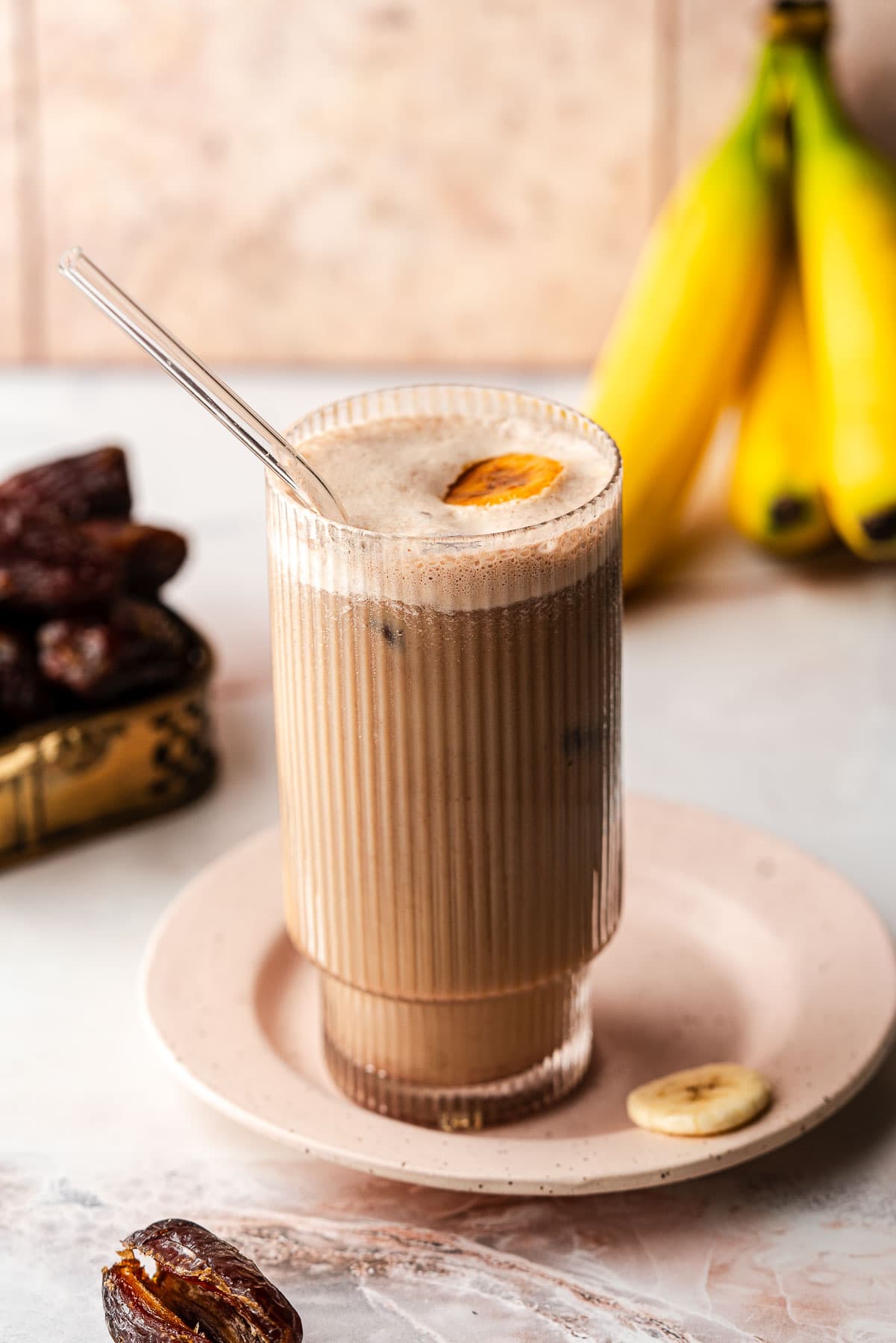 Banana Date Latte with a straw on a plate with dates and bananas.