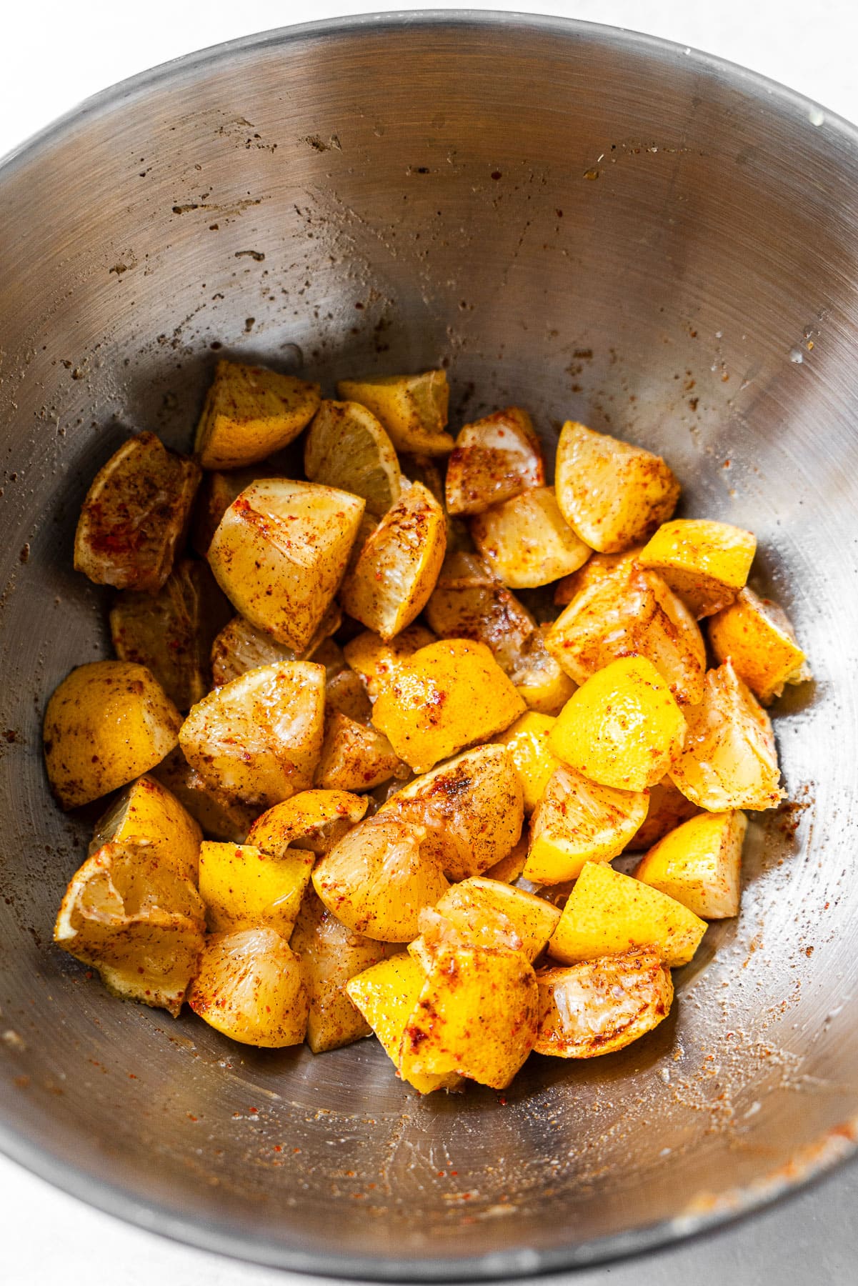 Quartered fresh lemons tossed in spices in a bowl.