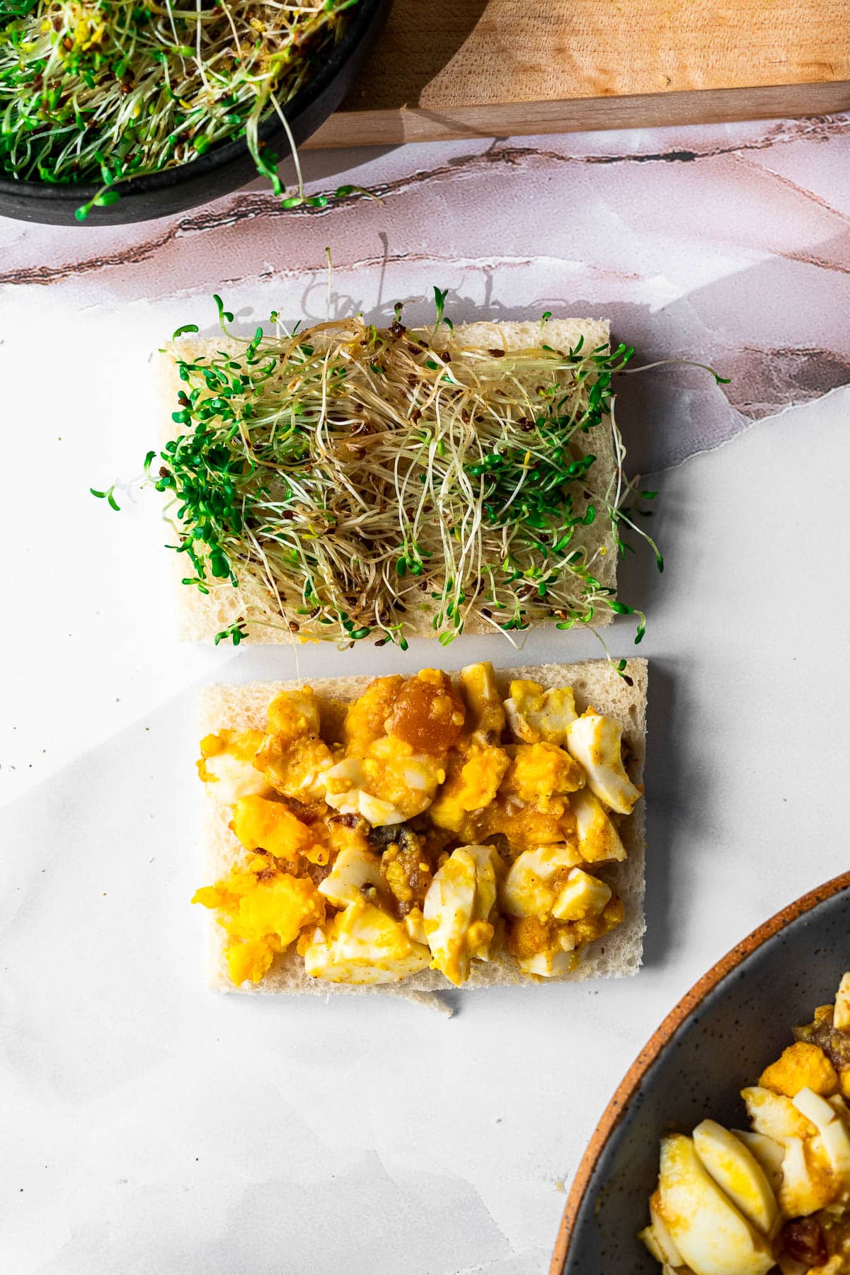 crustless white bread slices with chutney egg salad on slice and sprouts on another sandwich