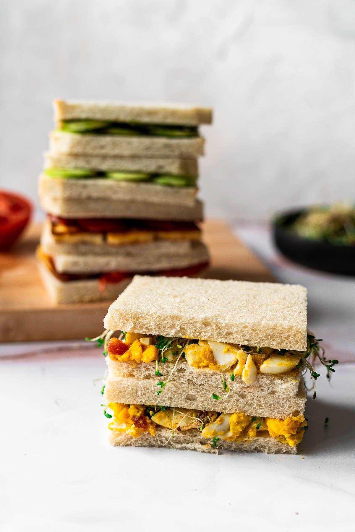 chutney egg salad tea sandwich in the forefront of the photo with stacked tea sandwiches in the back