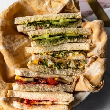 three tea sandwiches sliced into diagonals and stacked on top of each other in a bowl with yellow linen