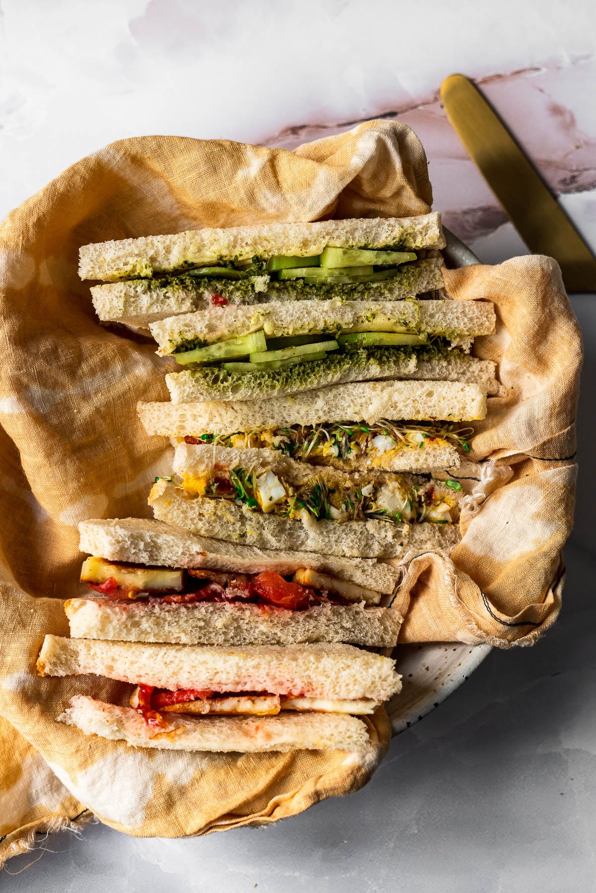 three tea sandwiches sliced into diagonals and stacked on top of each other in a bowl with yellow linen