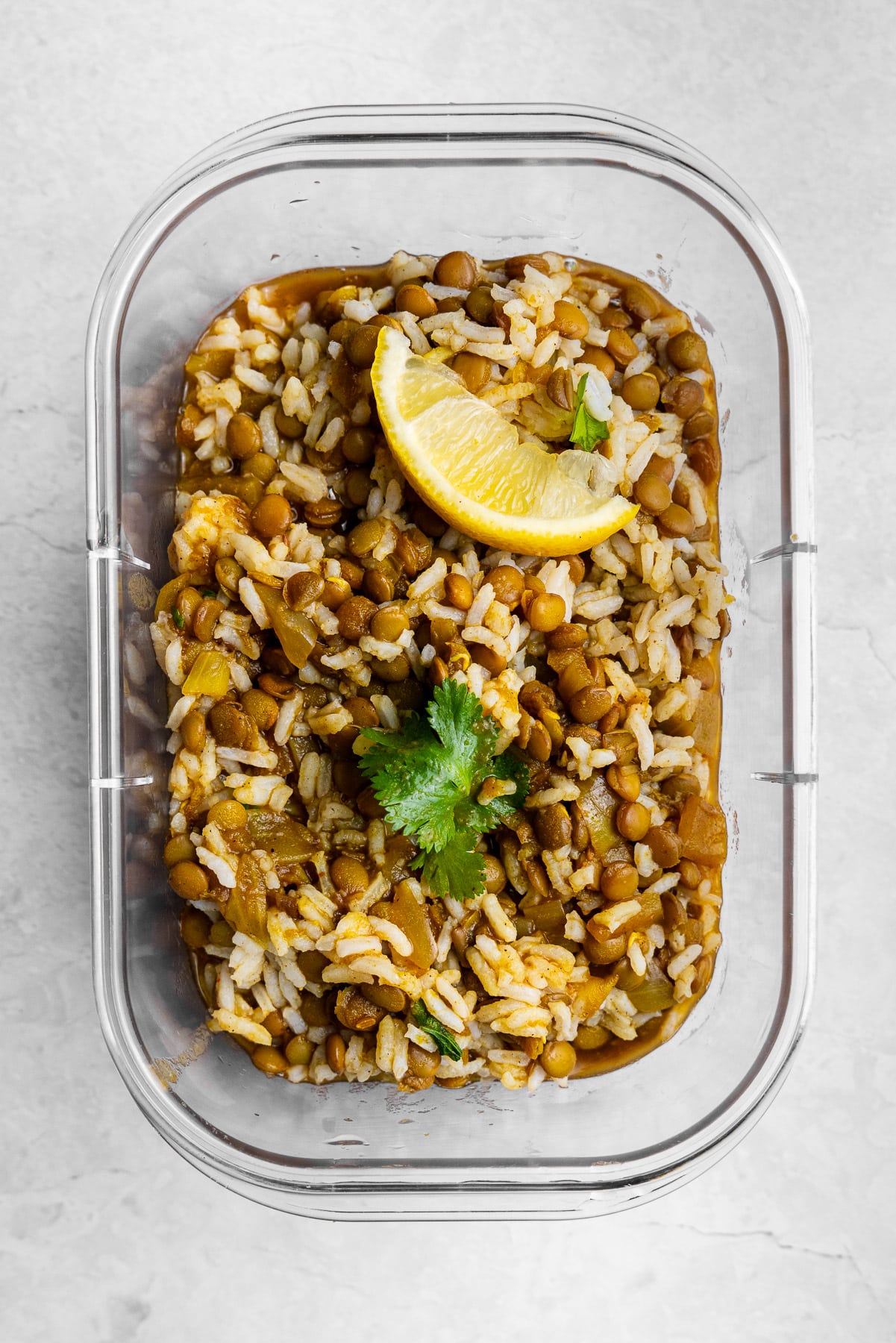 masoor dal mixed with rice, cilantro, with a lemon wedge in a meal prep container.