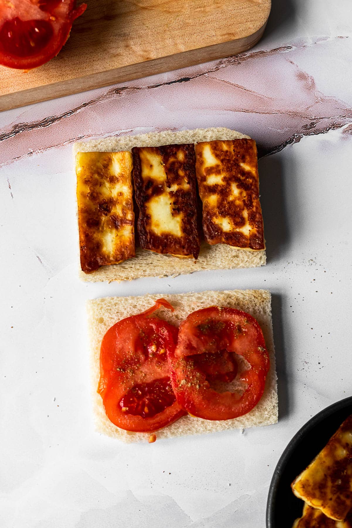 crustless white bread slices with fried paneer on one slice and tomato with chaat masala on the other slice