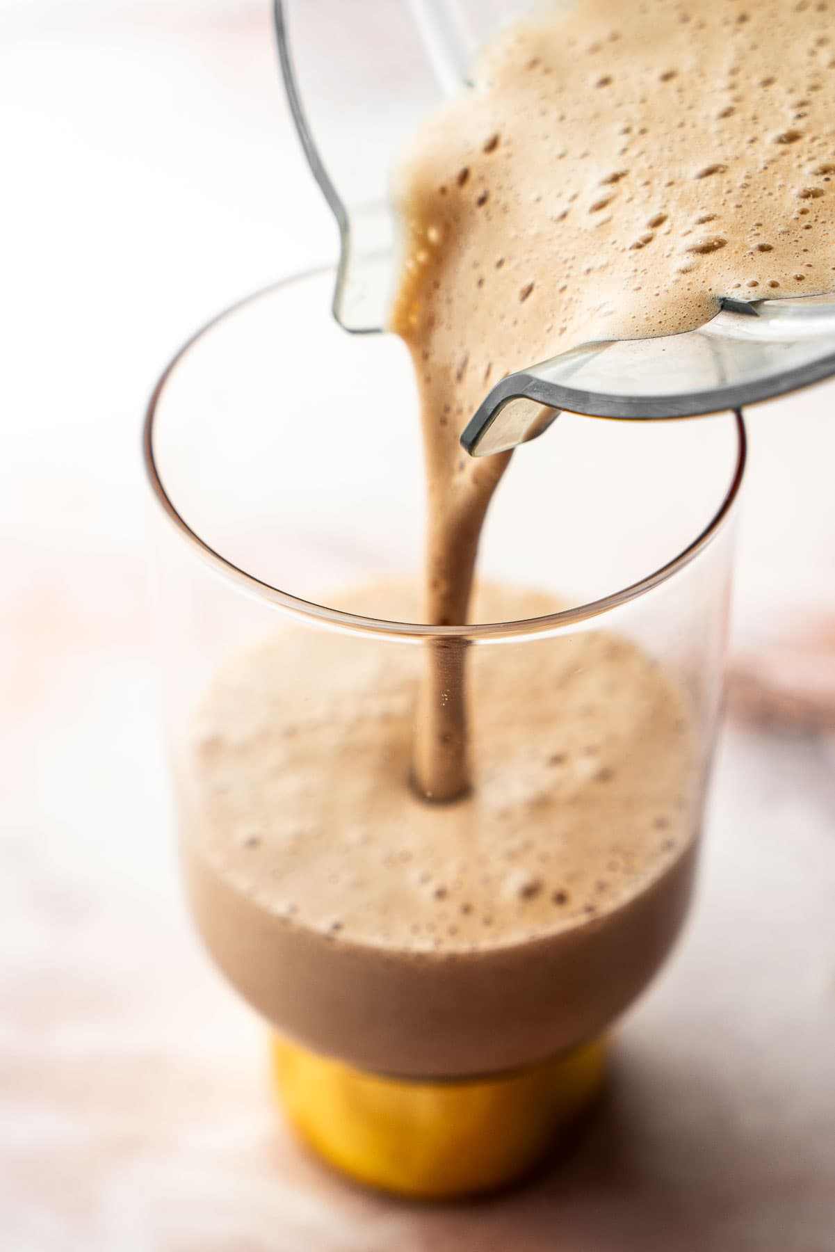 Pouring banana date latte into a tall glass from a blender.