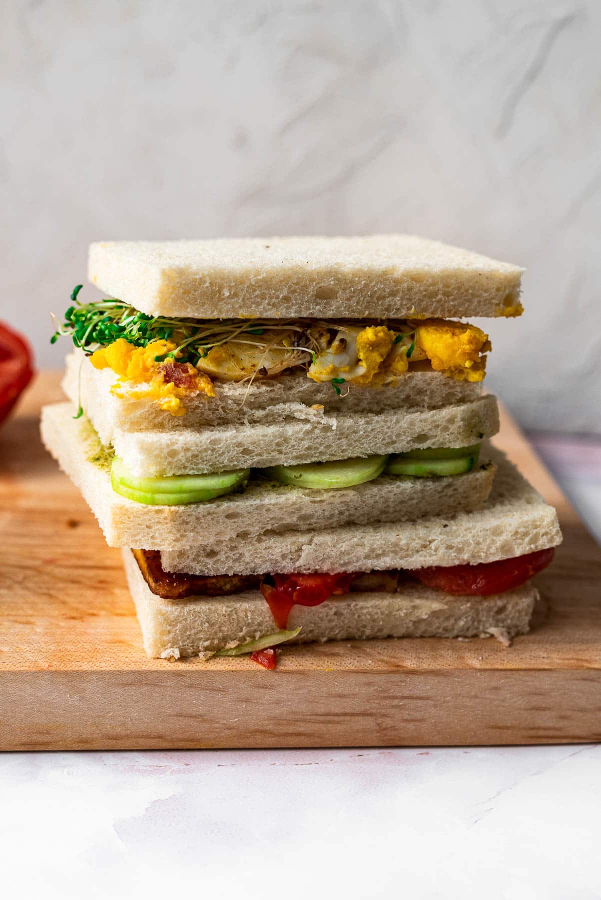 three tea sandwiches stacked on top of each other on a wooden board