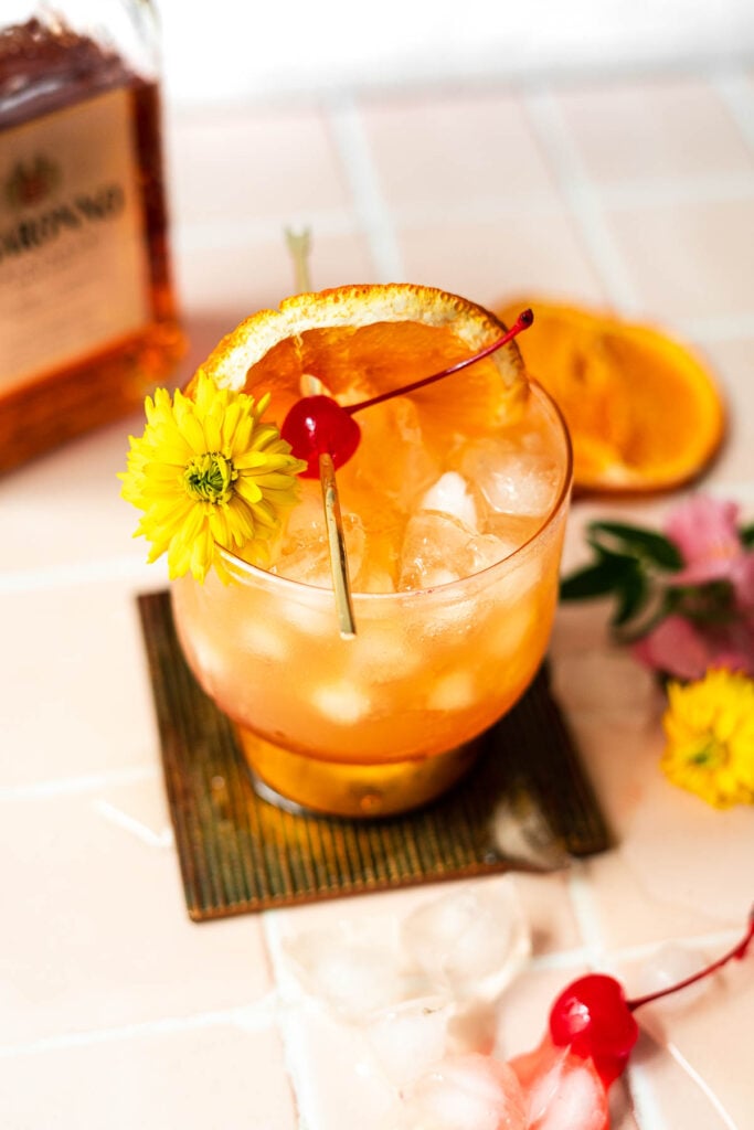 amaretto sour with bottle of alcohol in the back and garnishes next to it