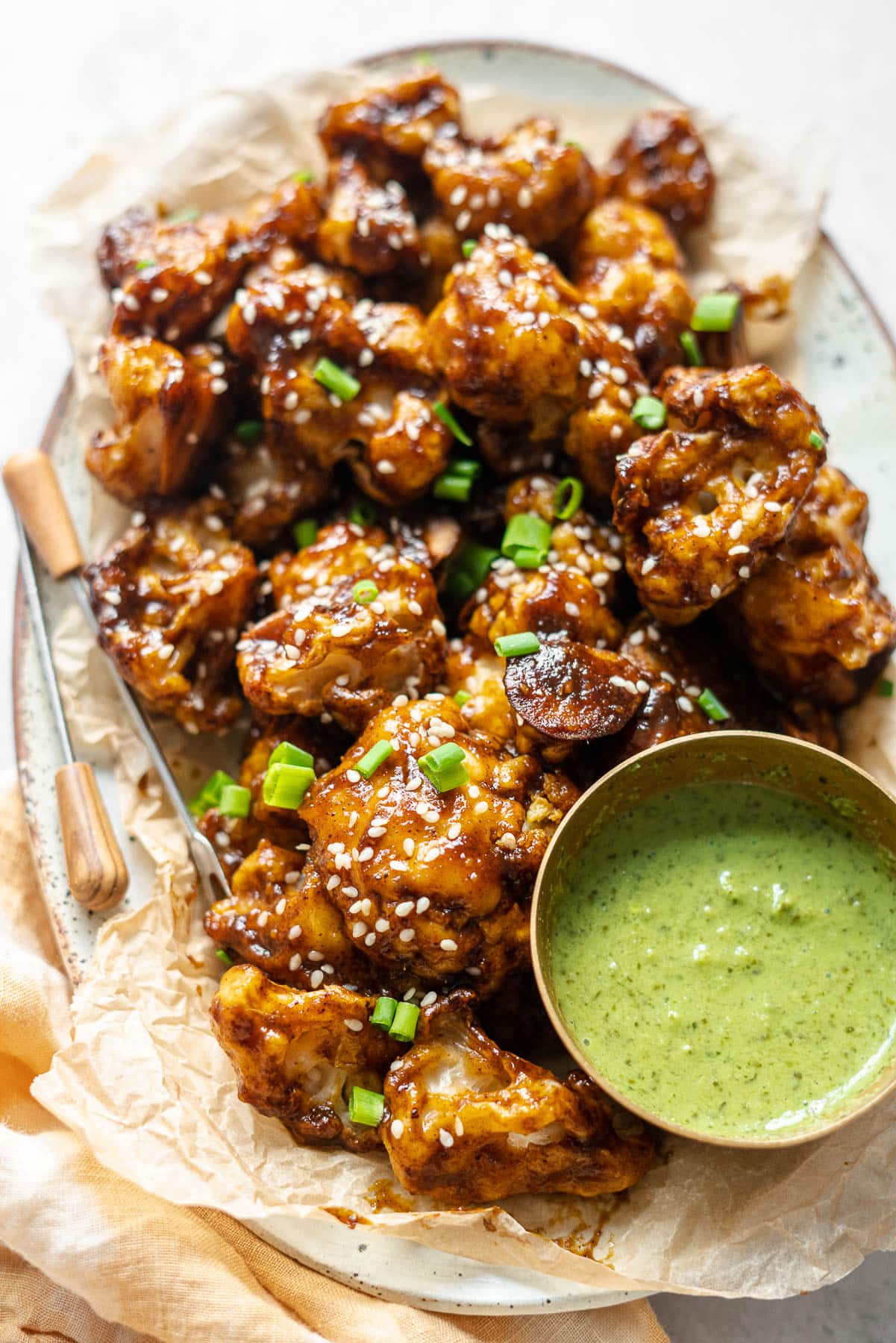 Close up Back Lit photo of cauliflower wings in a platter with appetizer picks and a condiment bowl of mint-cilantro chutney.