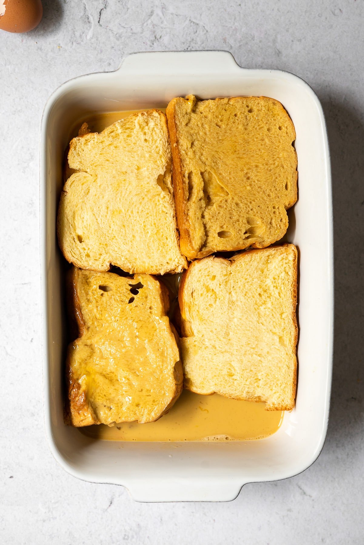 stuffed brioche french toast dipped in an egg mixture in a large white baker