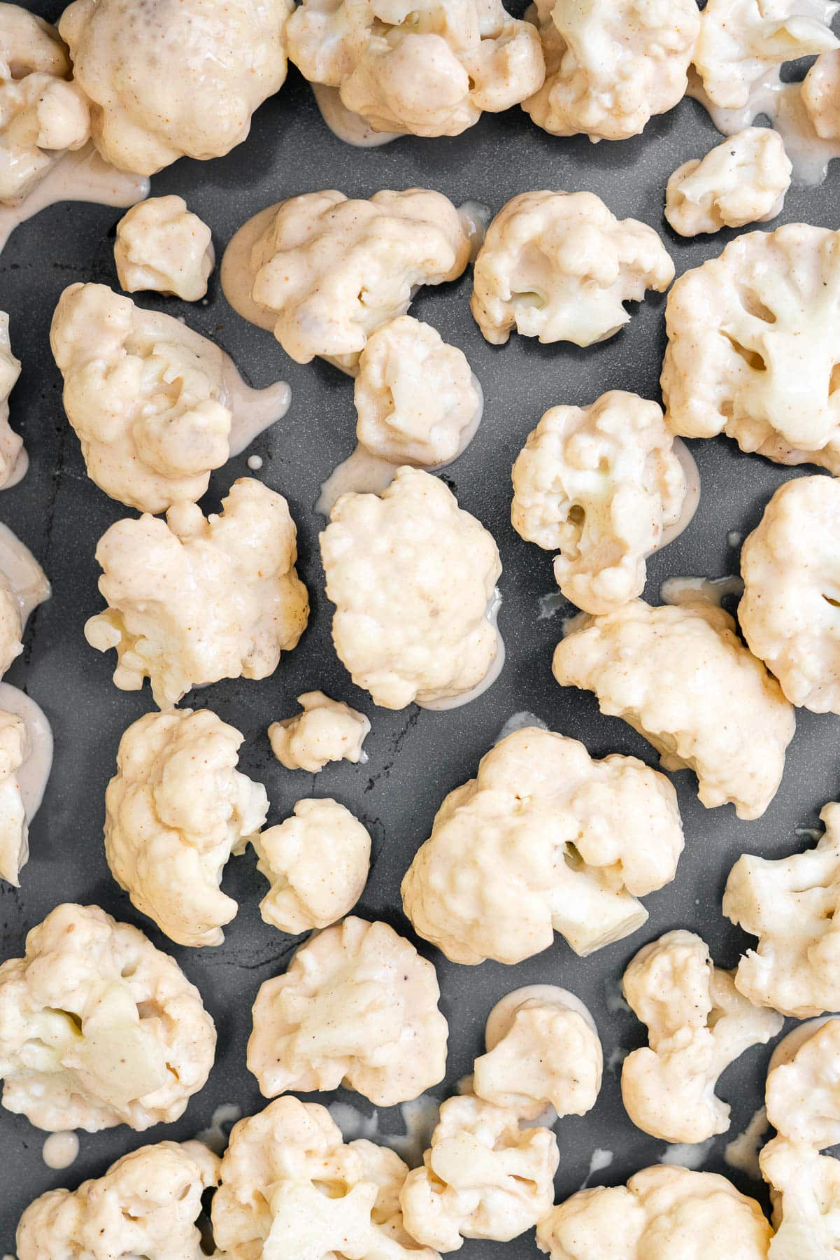 cauliflower florets coated in batter on a sheet tray, ready to be baked
